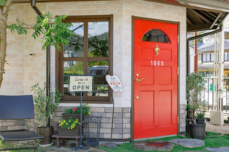「Come In We're OPEN」の看板が置かれた、チロリア八鹿店の赤いドア