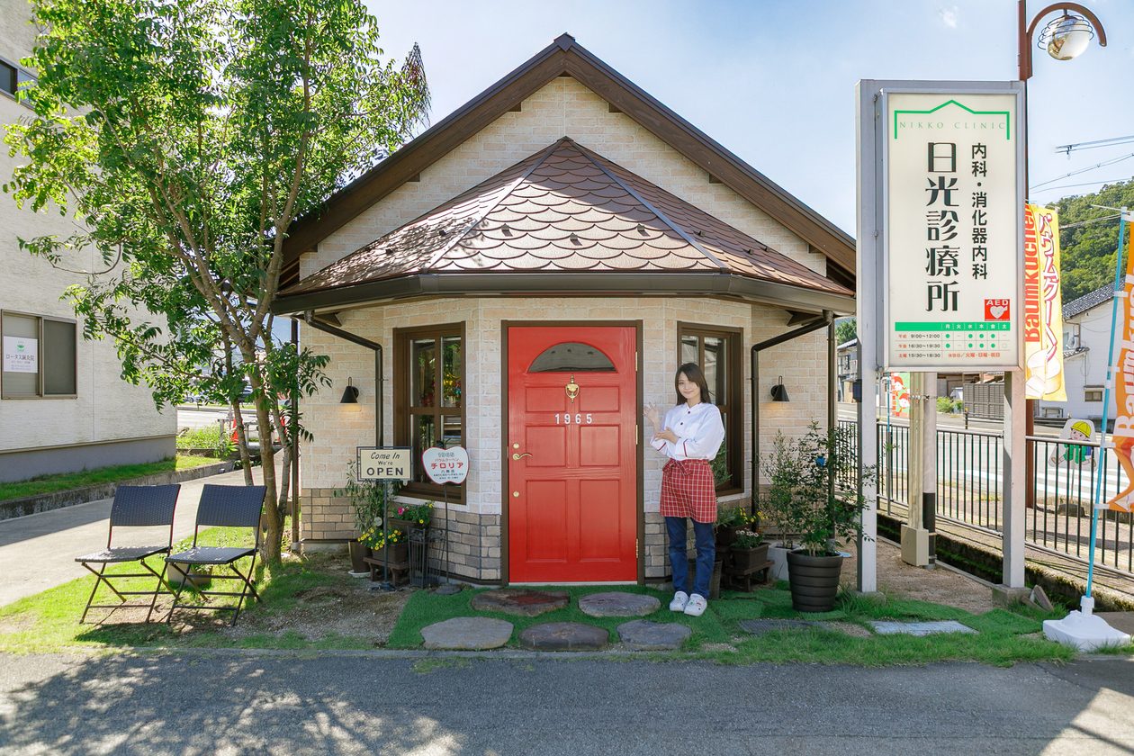 日光診療所の敷地内に建つチロリア八鹿店の外観。赤いドアの前に立つ店員
